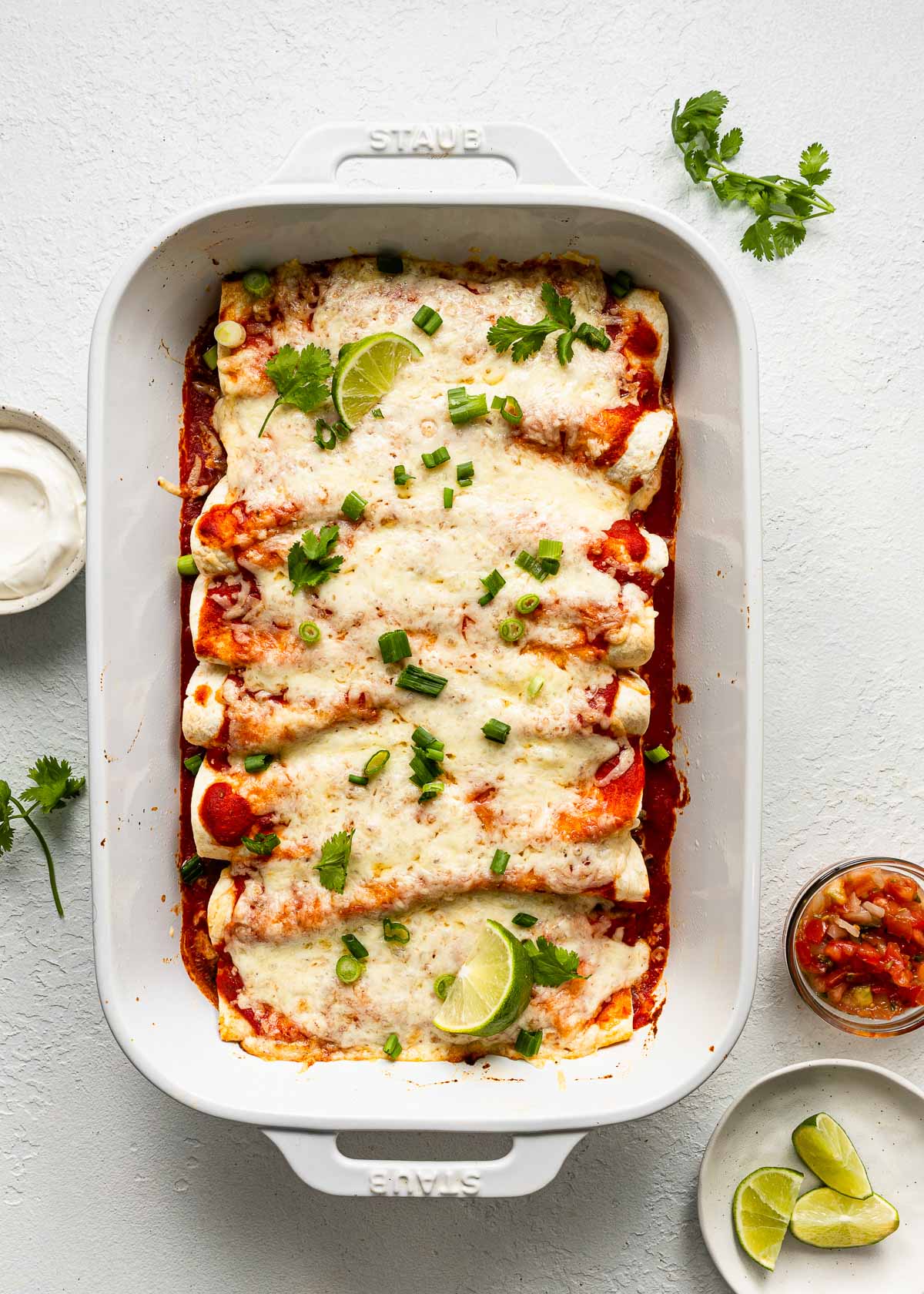 overhead view of a white baking dish filled with beef enchiladas on white surface.