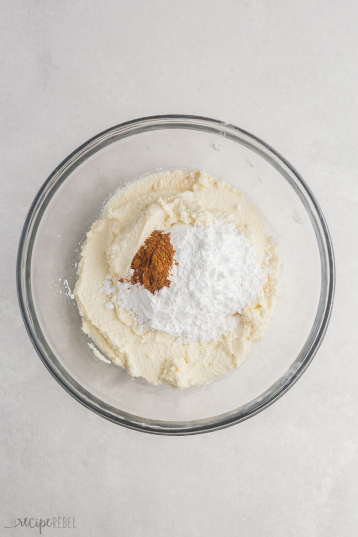 glass mixing bowl with unmixed cannoli, powdered sugar, and cinnamon.