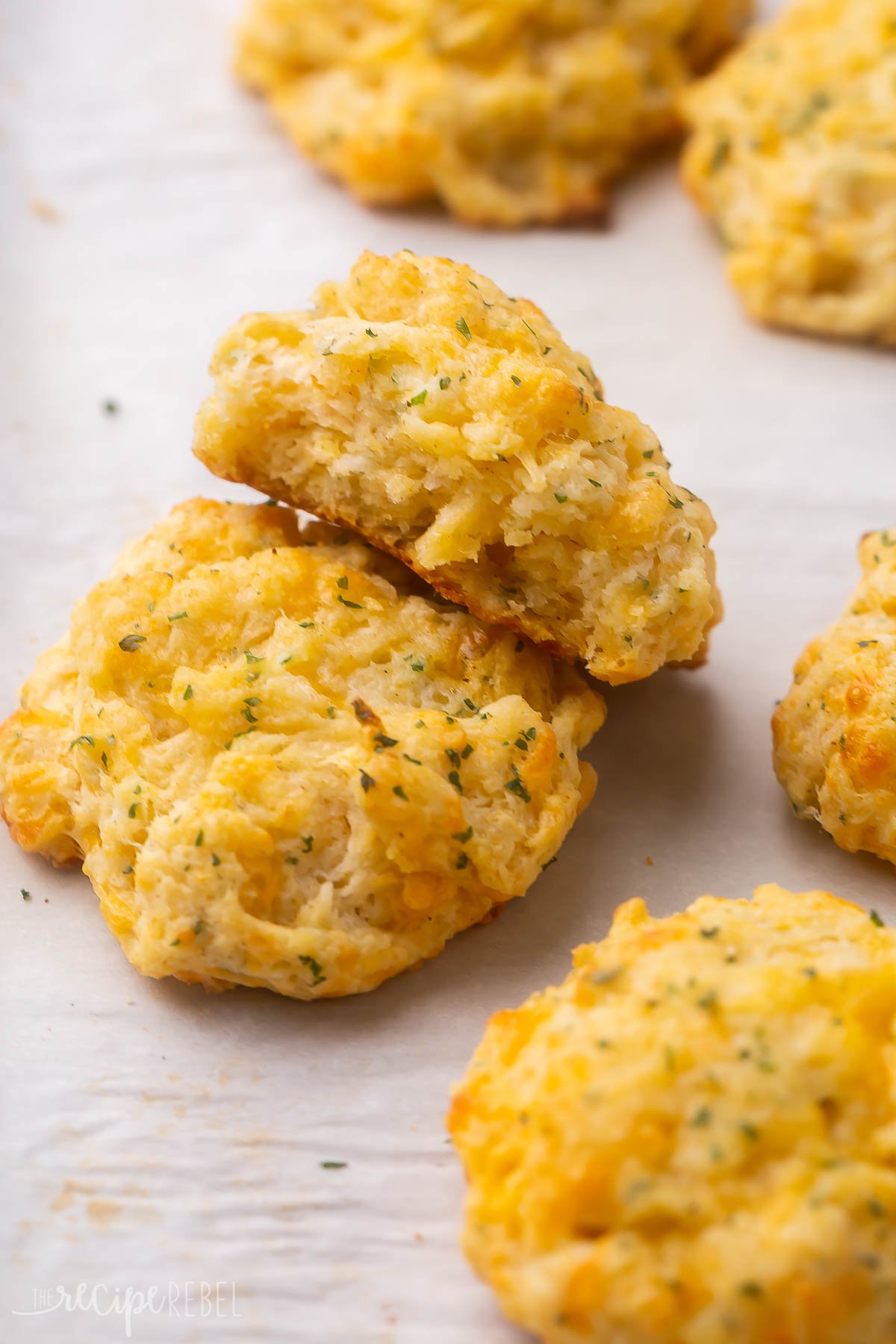 These Copycat Cheddar Bay Biscuits will be one of the best things to grace your dinner table! Made with homemade biscuit dough topped with garlic butter, these delicious biscuits are baked to perfection with a crisp outer while remaining soft and fluffy on the inside! #biscuits #baking #recipes | biscuit recipe | cheese biscuits | cheddar biscuit | drop biscuits | easy biscuits a few cheddar bay biscuits lying on parchment paper.