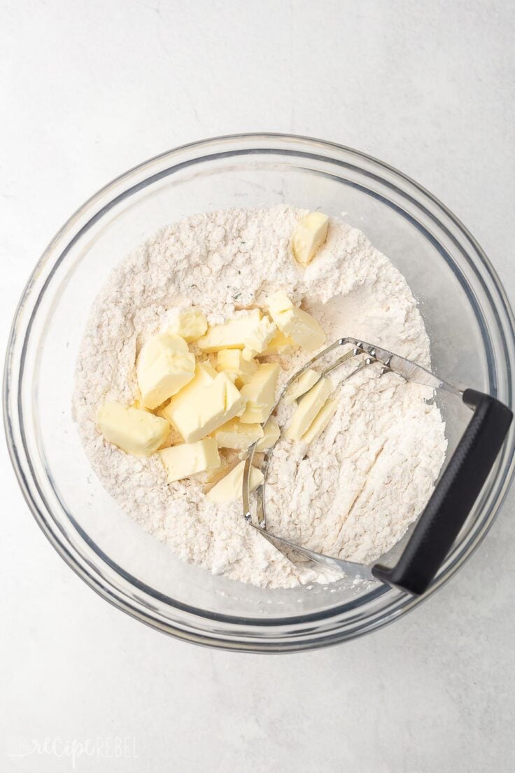 cubed butter on top of mixed dry ingredients in glass bowl.