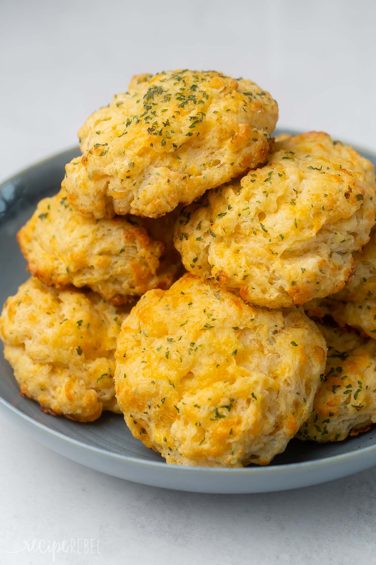 a dark grey plate stacked up with cheddar bay biscuits.