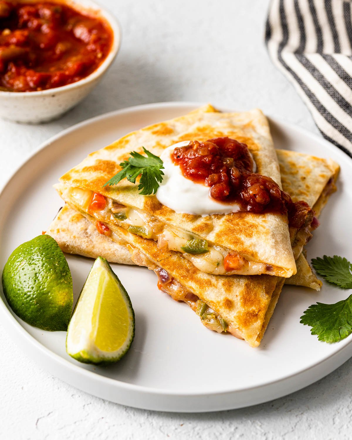 three cheese quesadillas on a white plate topped with salsa and sour cream.