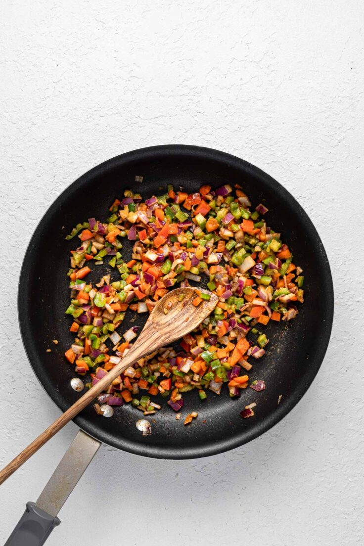 black frying pan with cooked chopped vegetables and a wooden ladle.