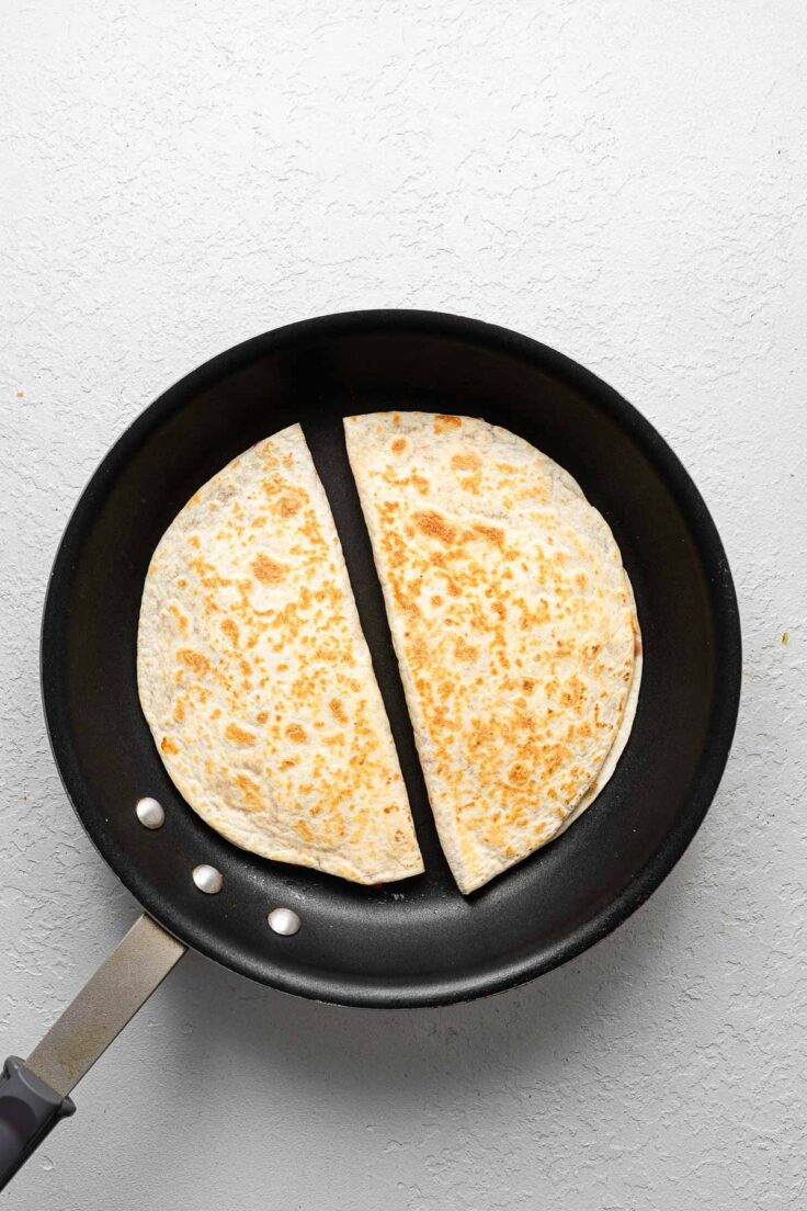 two cooked cheese quesadillas lying in a frying pan.