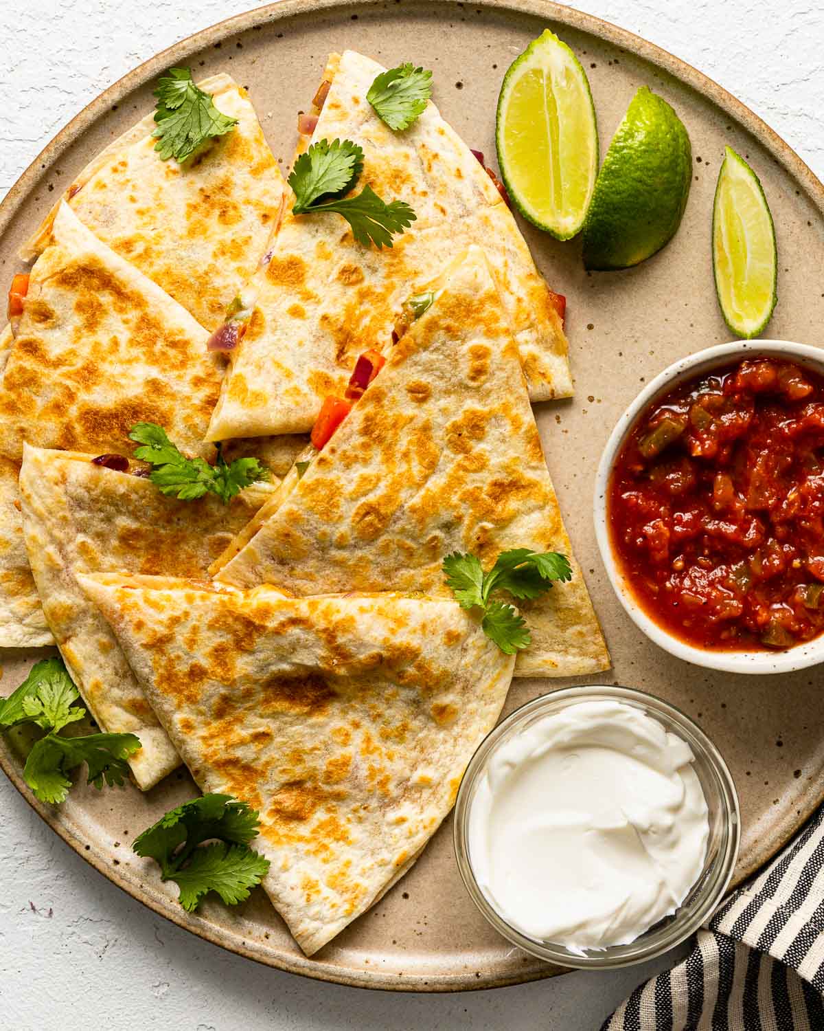 a large plate with cheese quesadillas, sour cream, salsa, and limes.