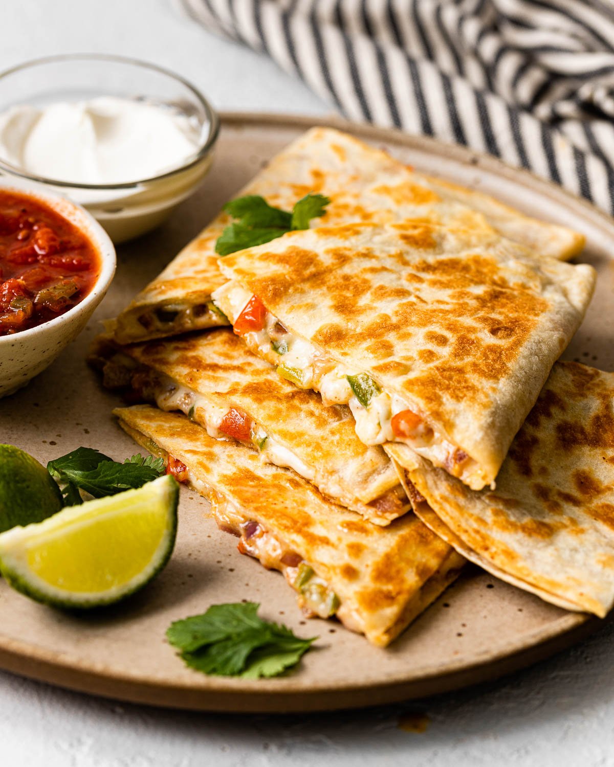 a stack of cheese quesadillas on a plate with salsa and sour cream beside.