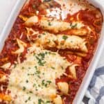 square image of red chicken enchiladas in white baking dish.