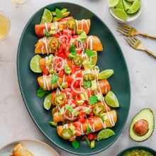 close up of a platter of chicken taquitos with toppings on a grey surface.