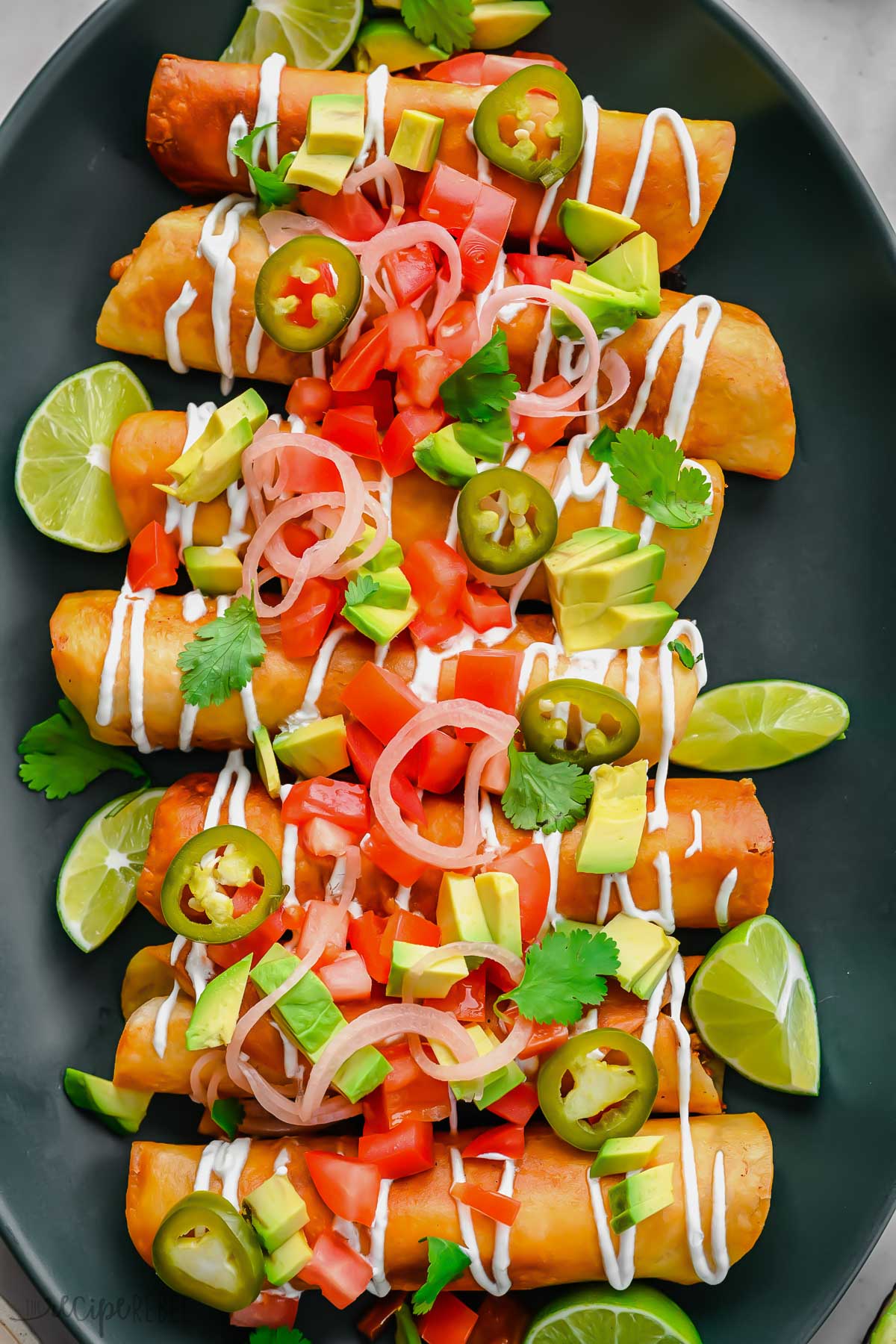 close up shot of chicken taquitos on a platter covered in toppings.