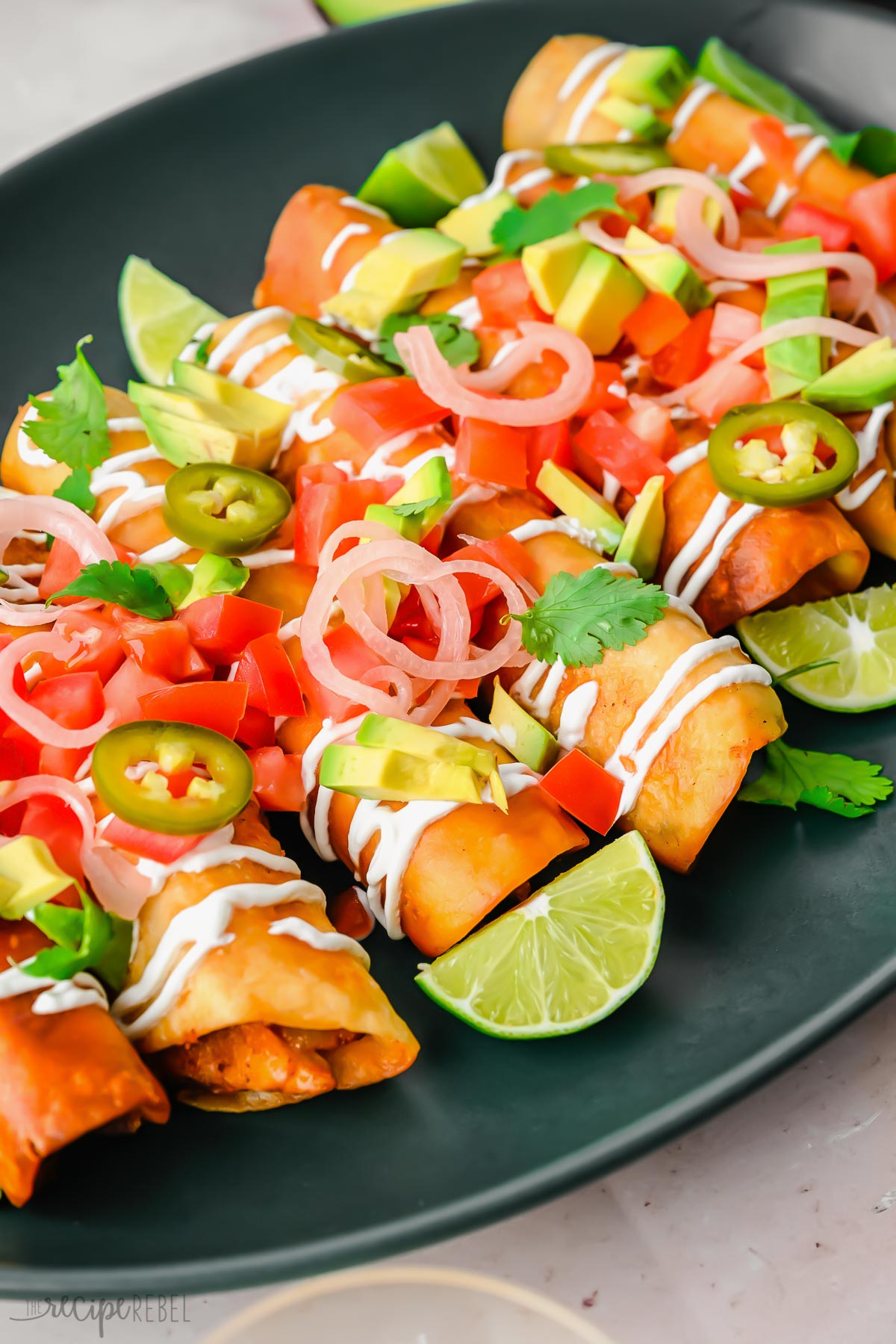 side view of chicken taquitos on a dark platter with toppings.