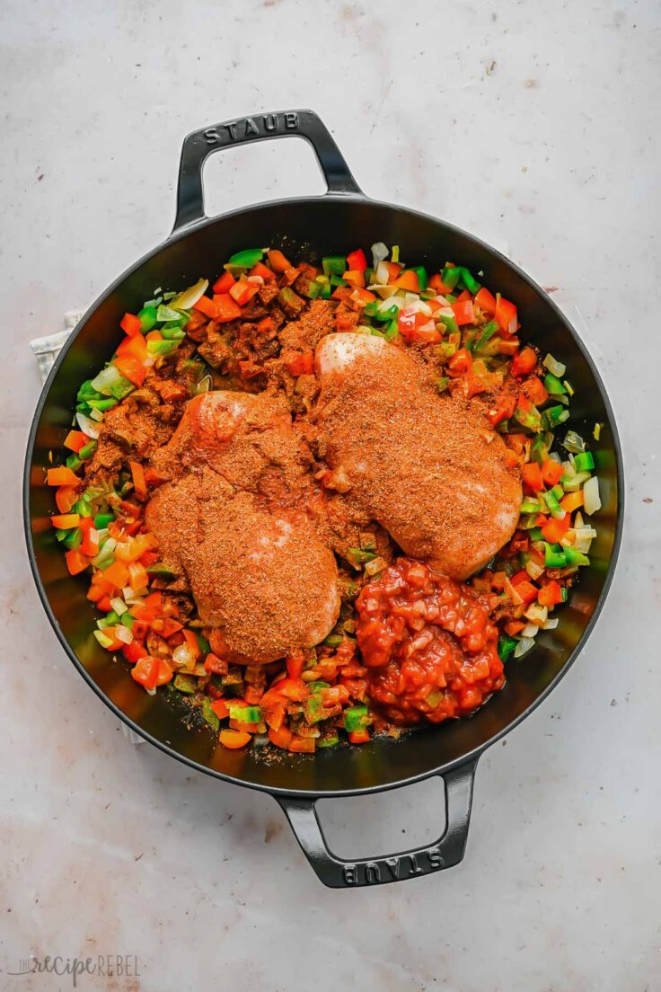black pan filled with vegetables and topped with seasoned chicken breasts and salsa.