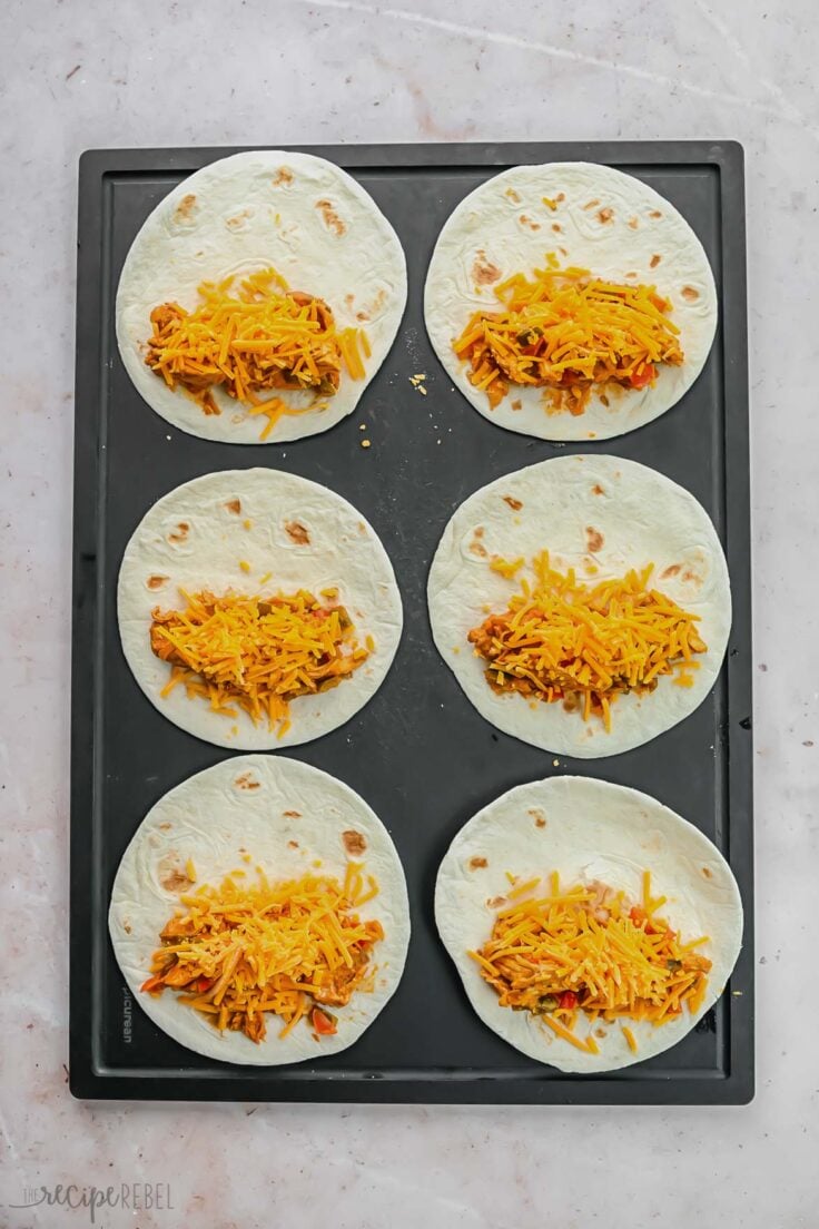 six tortillas open on a pan with filling and shredded cheese.