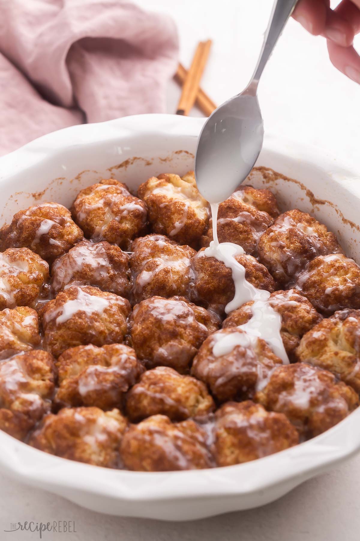 spoon drizzling glaze onto pan of cinnamon roll bites.