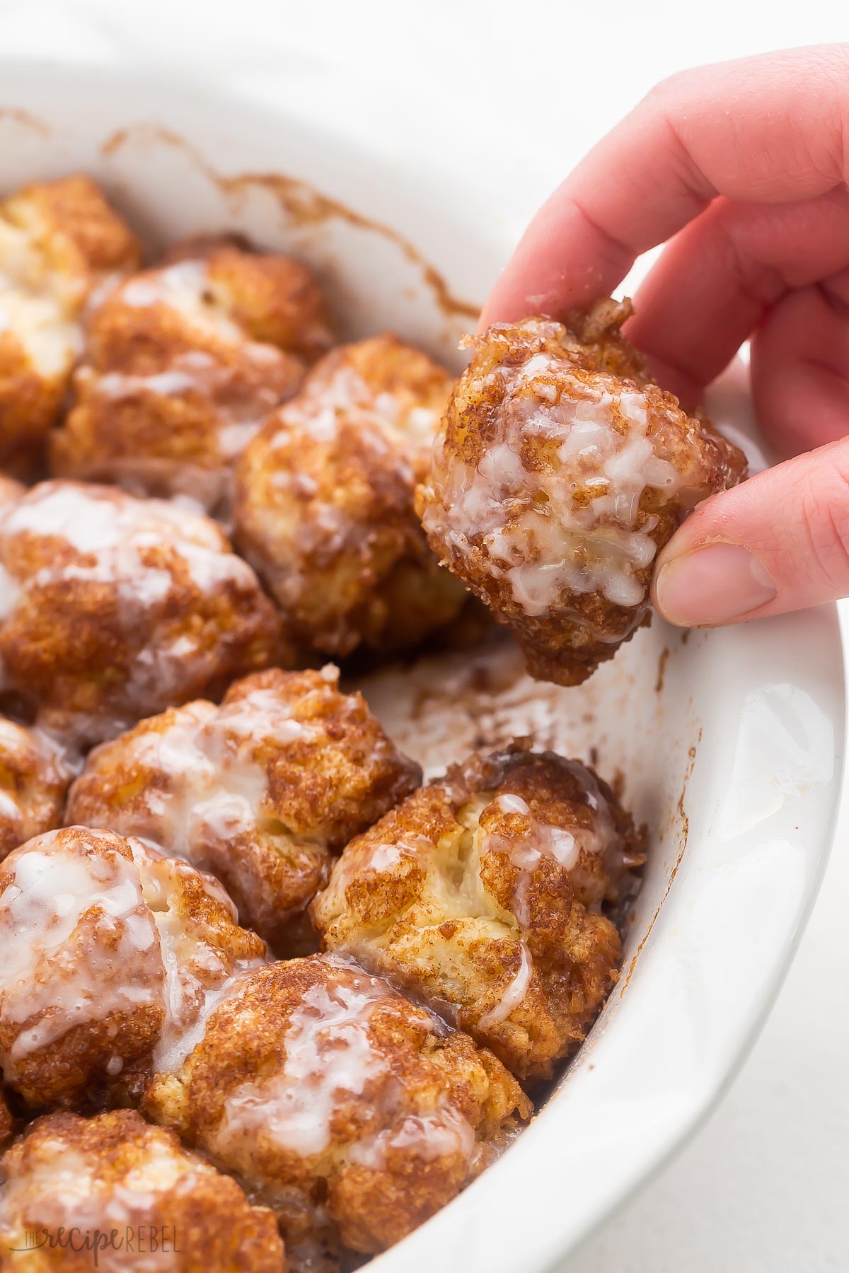 a hand pulling a cinnamon roll bite of a white dish.