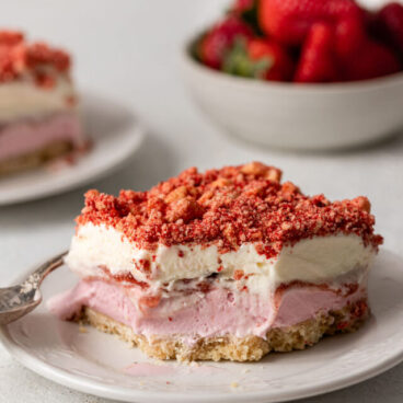 a plate with a piece strawberry shortcake ice cream bars and a bowl of strawberries in the background.