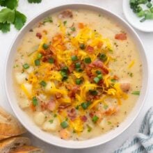 close up of a bowl of instant pot potato soup topped with cheese, green onions and bacon.