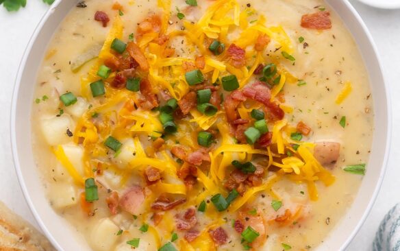 close up of a bowl of instant pot potato soup topped with cheese, green onions and bacon.