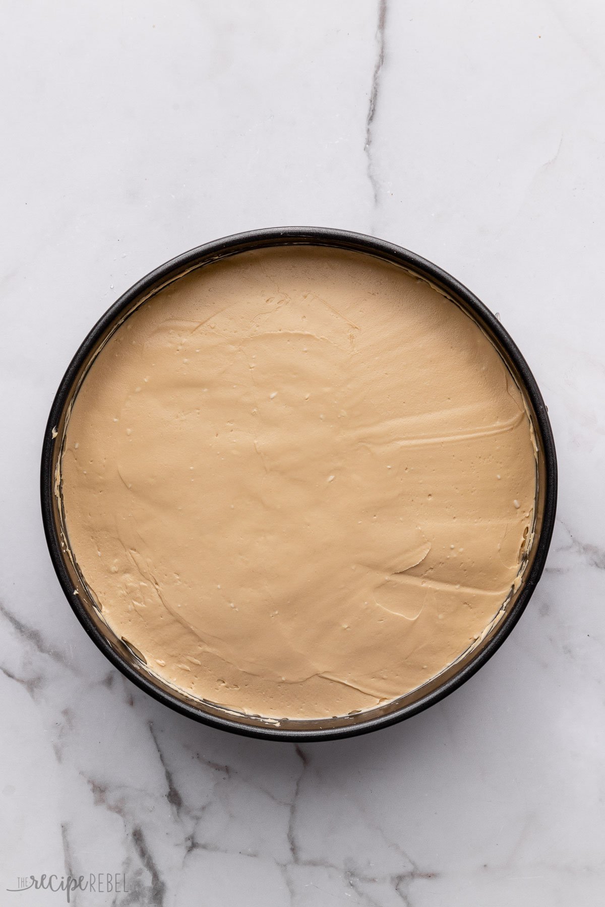 overhead shot of cheese cake spread into cake pan on grey surface.