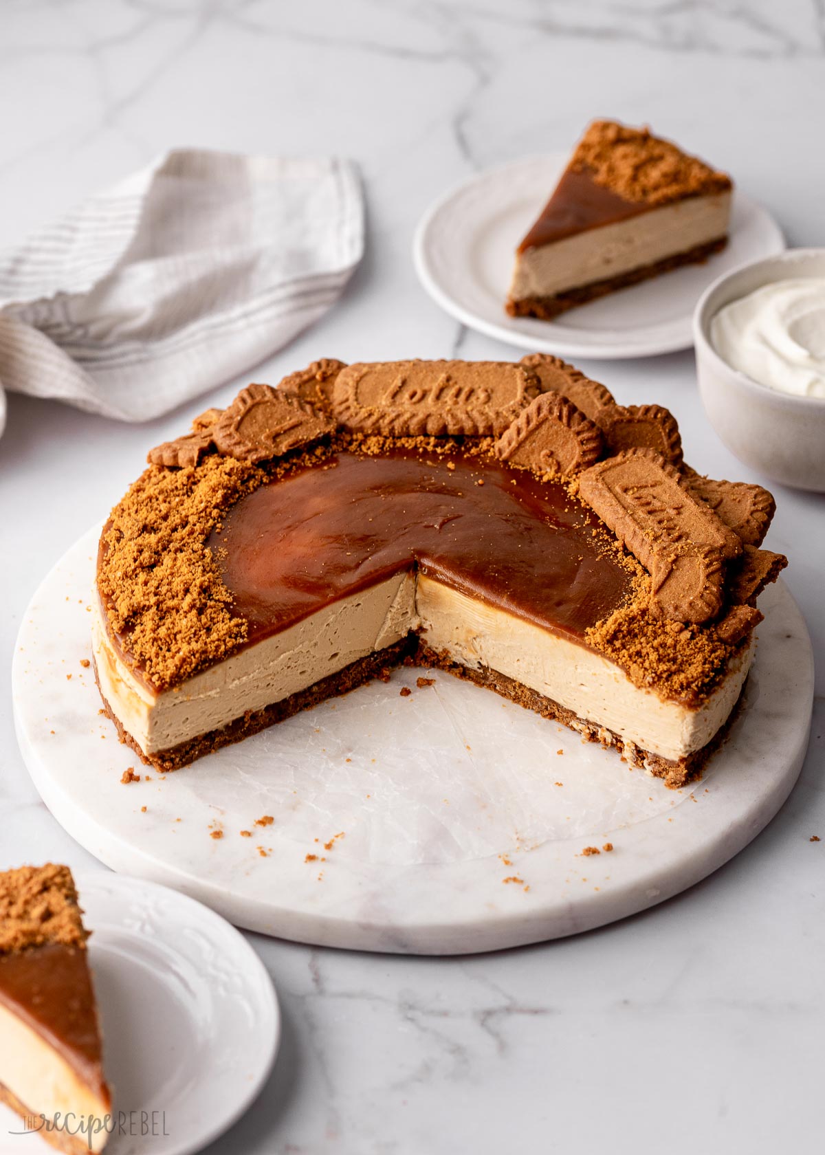 no bake biscoff cheesecake on a marble plate with pieces on white plates.