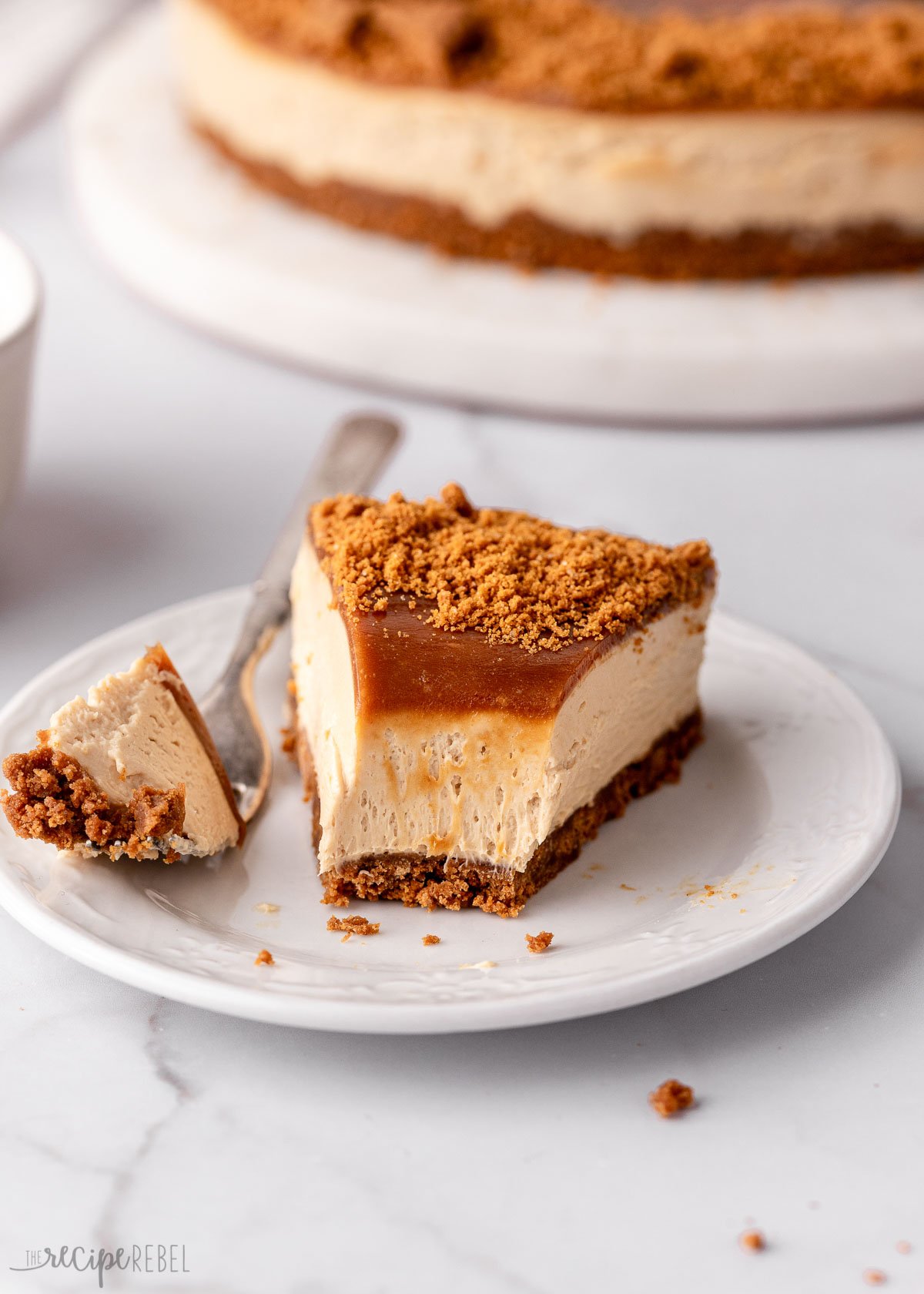 close up shot of a piece of cheesecake on a white plate with a fork beside.