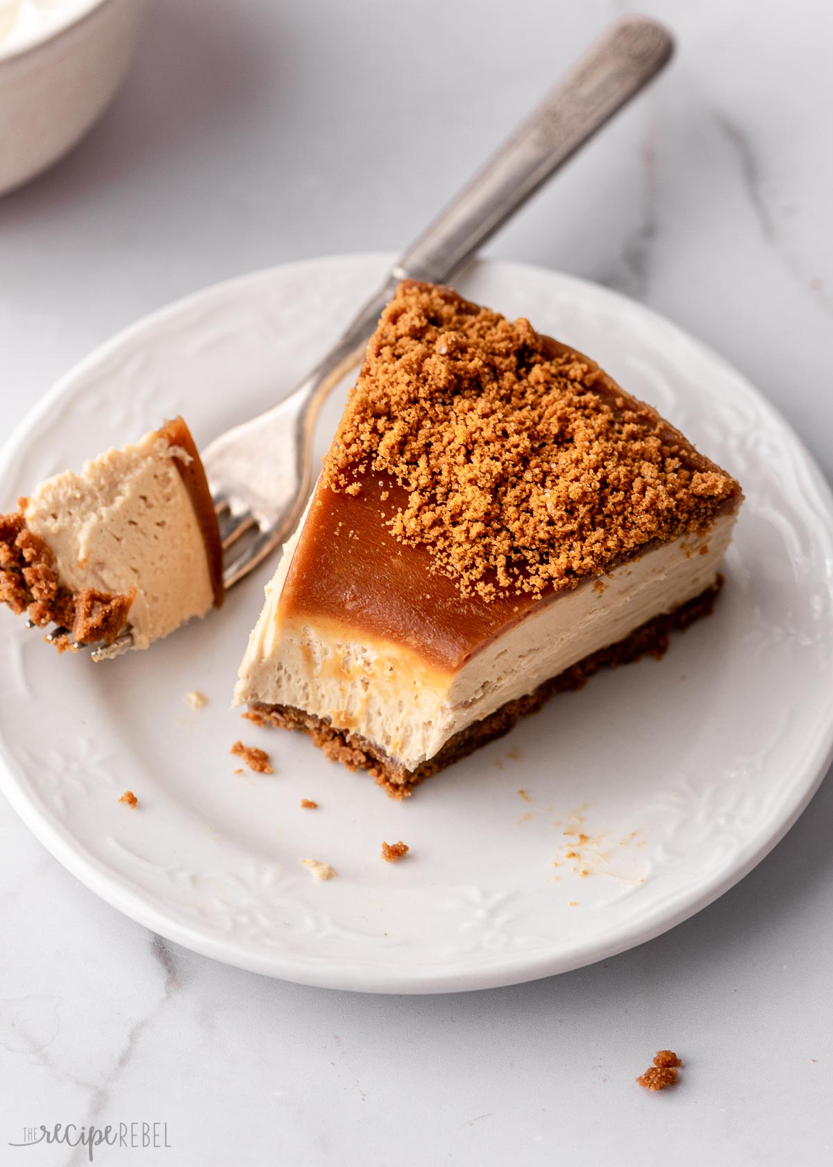 overhead shot of a piece of cheesecake on a white plate with a fork full beside.