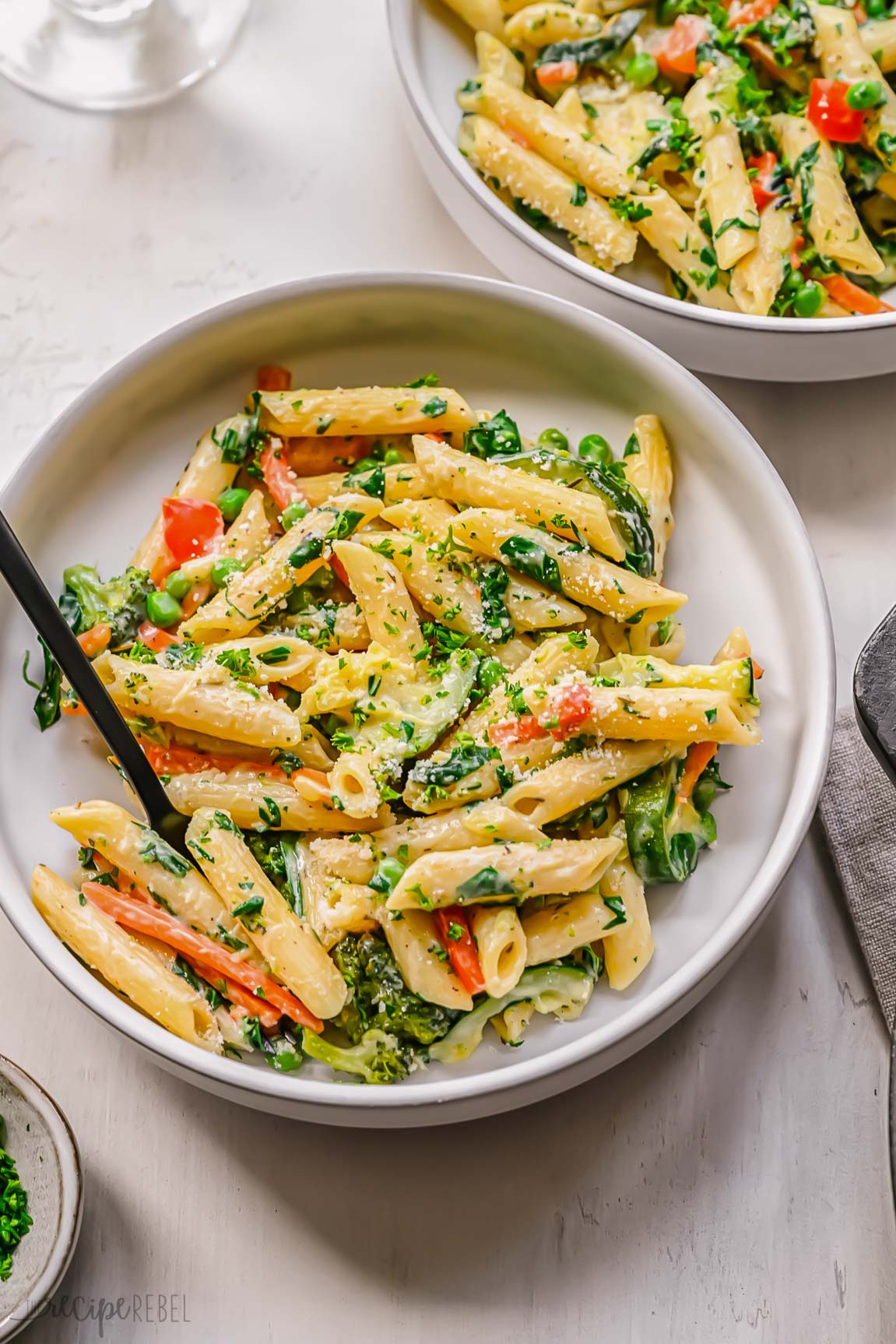 close up shot of a white plate with a fork and pasta primavera on it.