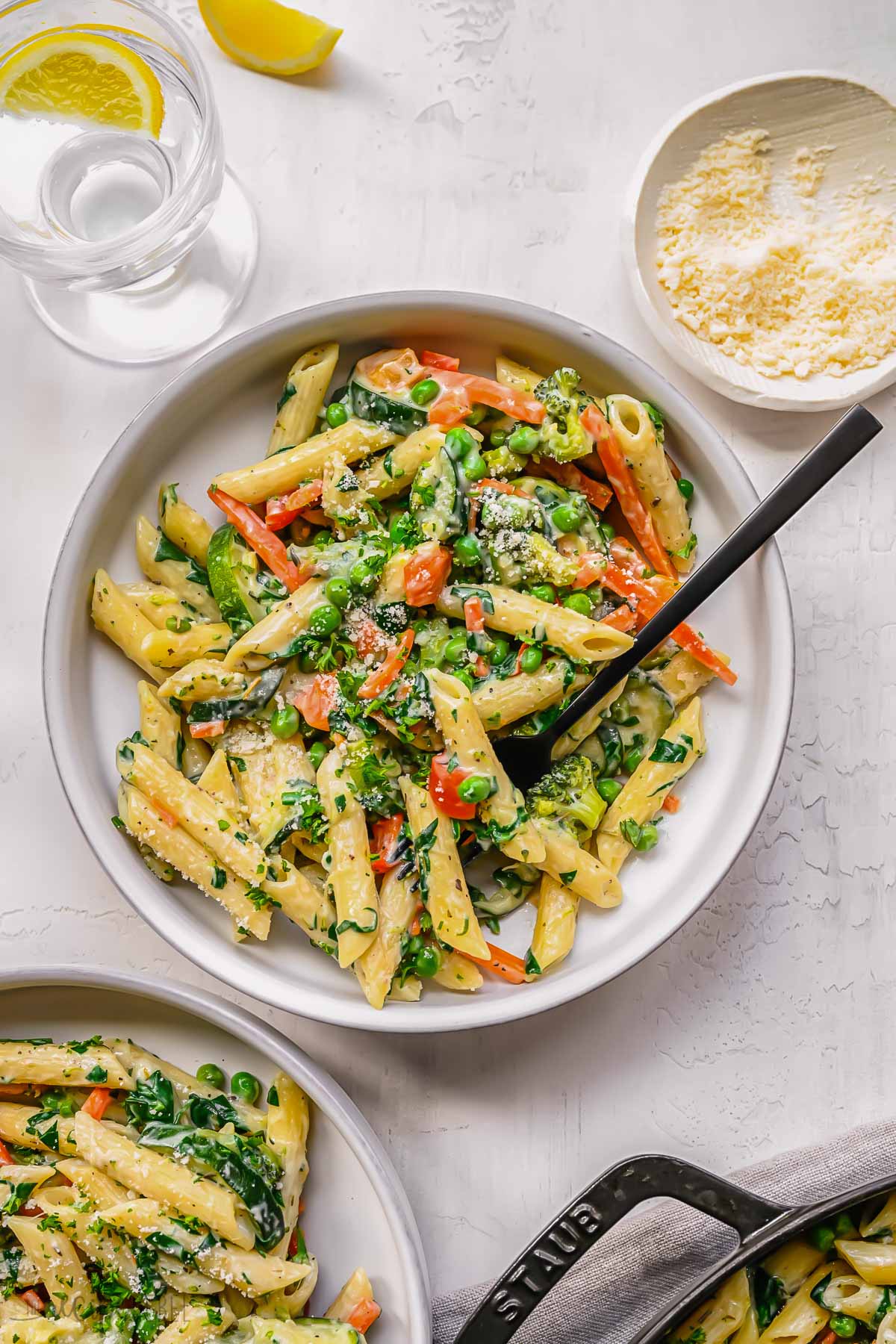 white plate filled with pasta primavera and a fork on white surface.