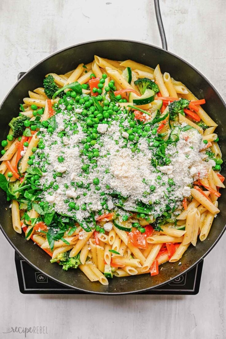 pan full of vegetables and pasta topped with peas and shredded parmesan cheese.