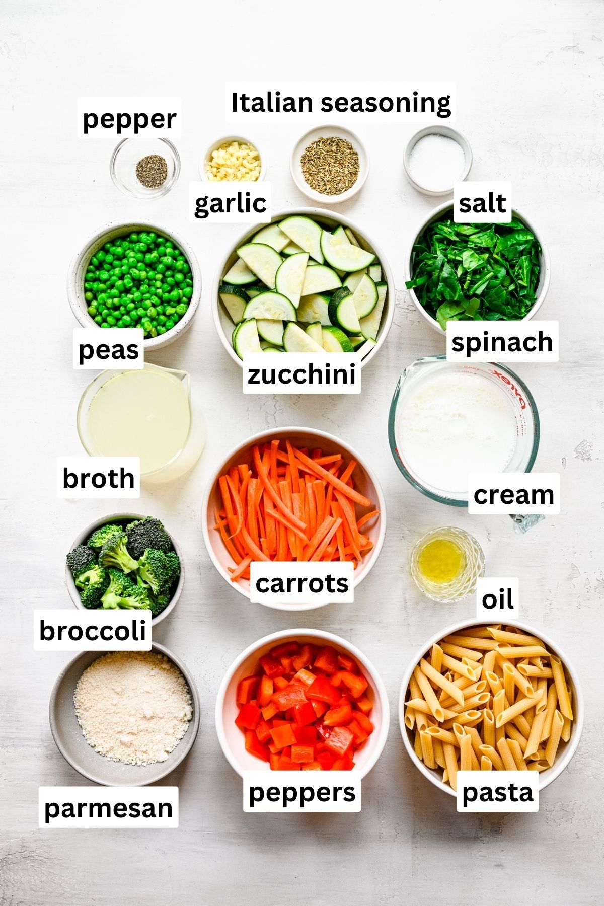 ingredients for pasta primavera in bowls on grey surface.