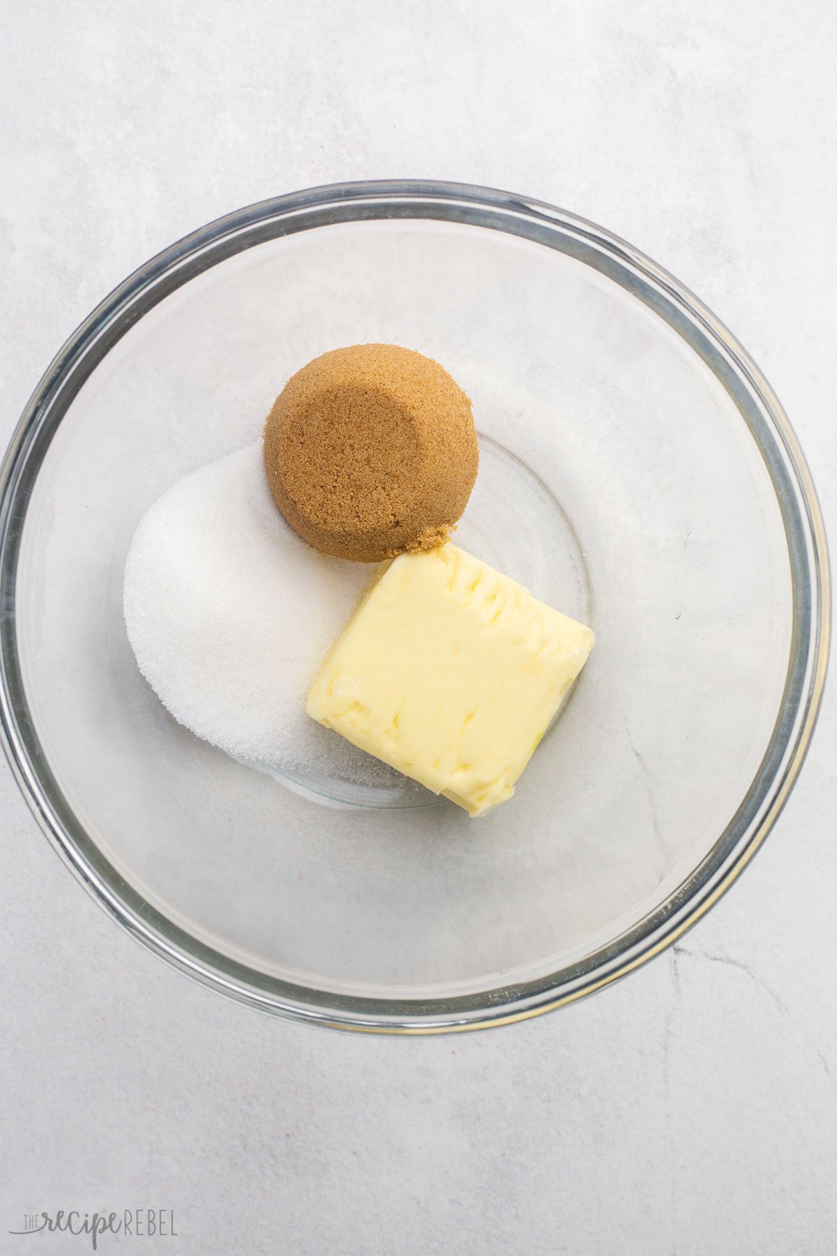 glass mixing bowl with sugar, butter, and brown sugar in it.