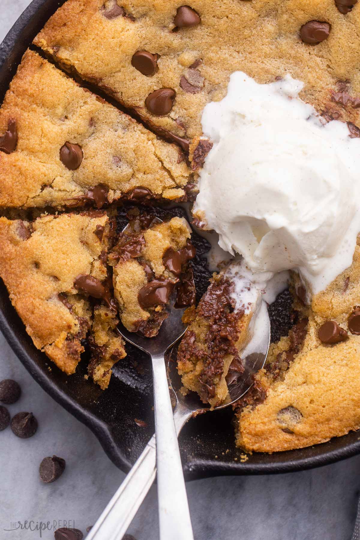 overhead shot of spoons in skillet cookie with a scoop of vanilla ice cream.