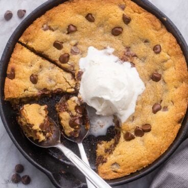 overhead close up of skillet cookie in pan with spoons and vanilla ice cream on top.