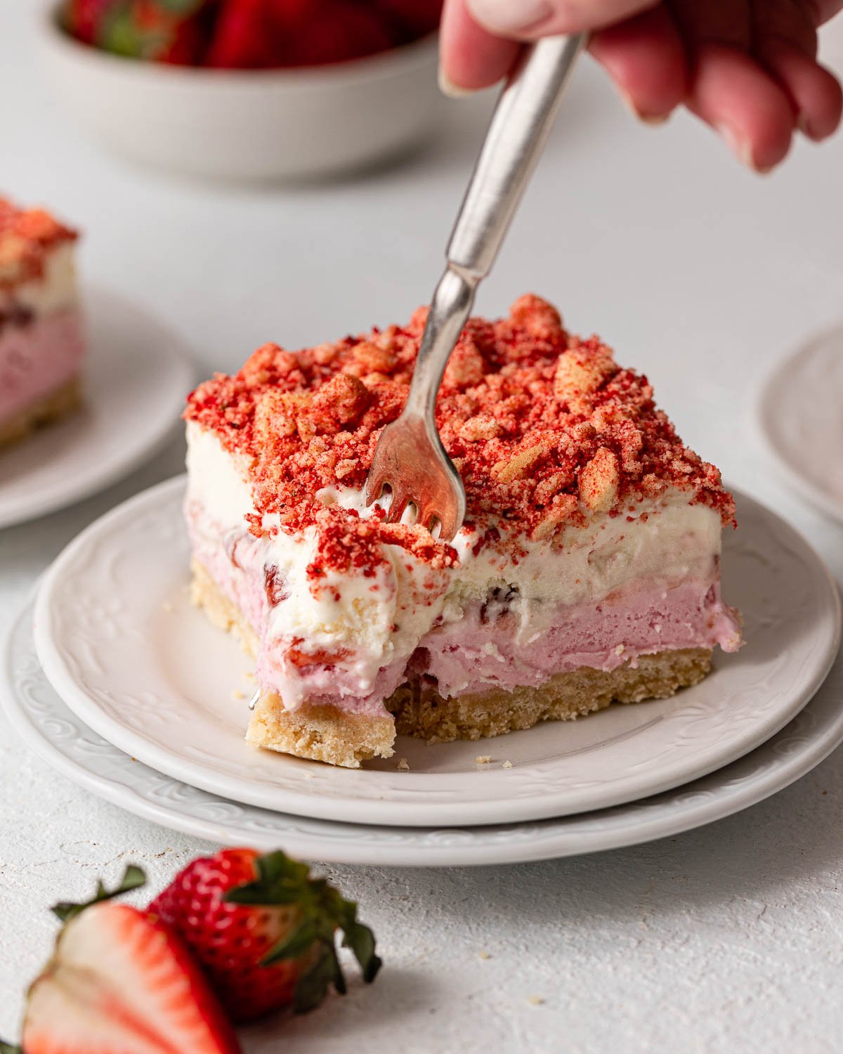 a fork scooping a bite of a strawberry shortcake ice cream bars on a white plate.