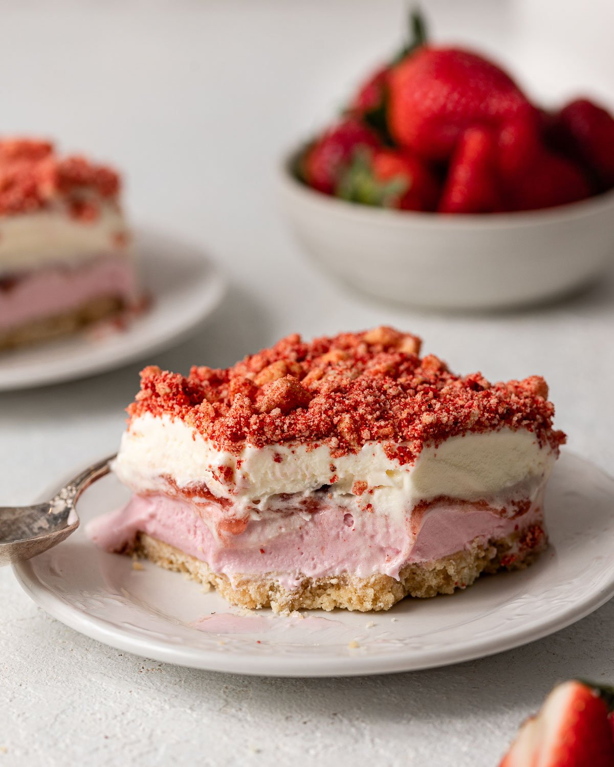 a plate with a piece strawberry shortcake ice cream bars and a bowl of strawberries in the background.