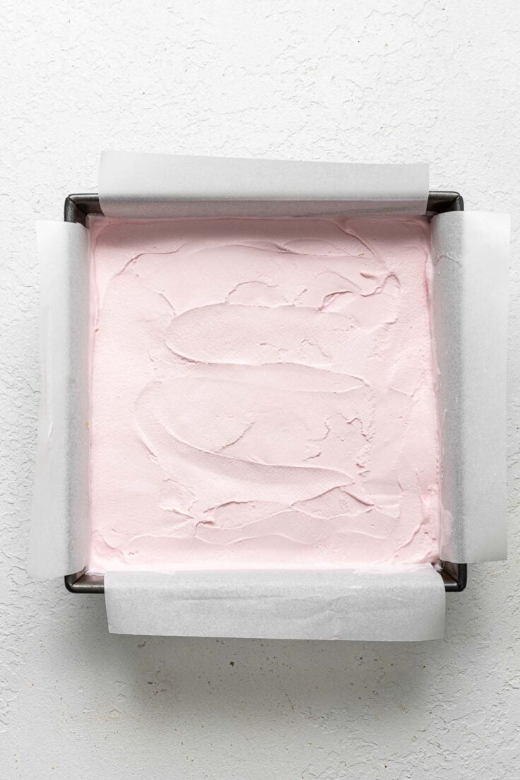 overhead shot of lined cake pan with strawberry ice cream evenly spread in it.