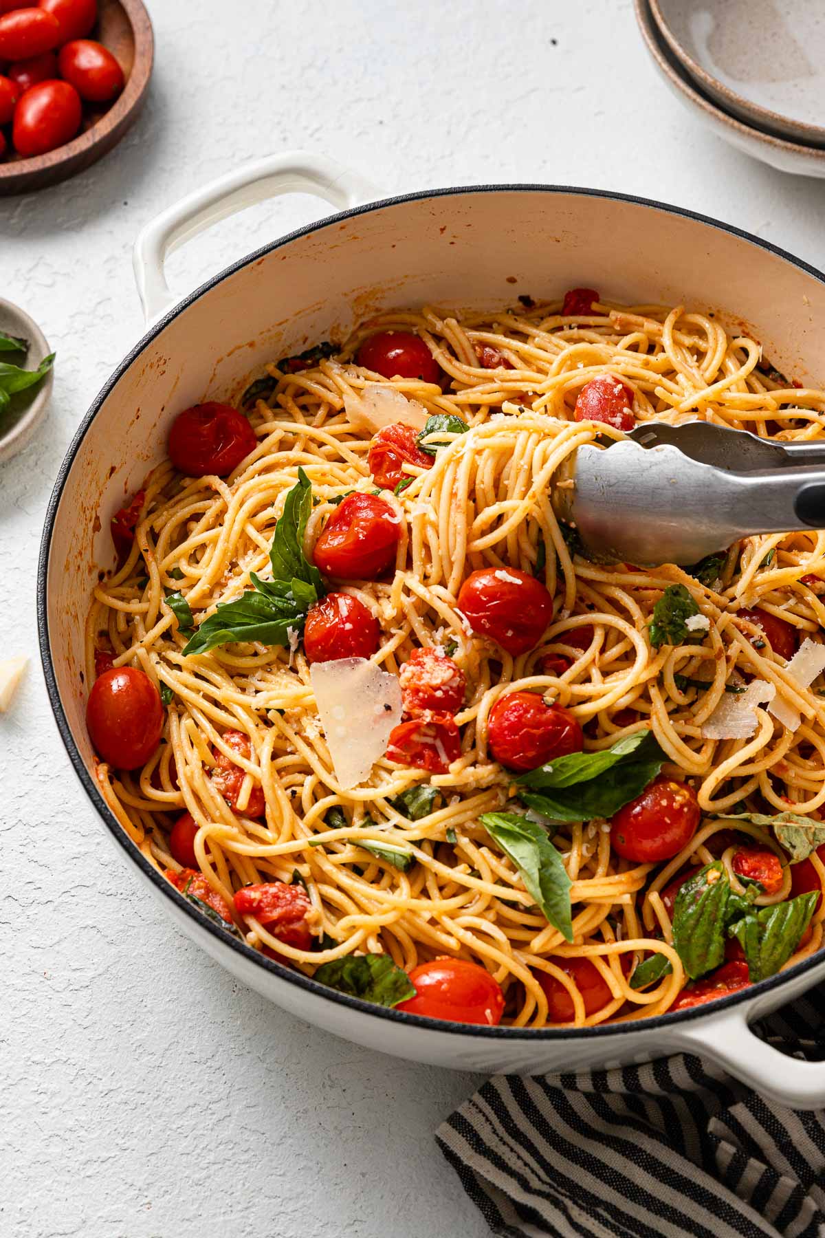 steel tongs pulling tomato basil pasta out of white pan.