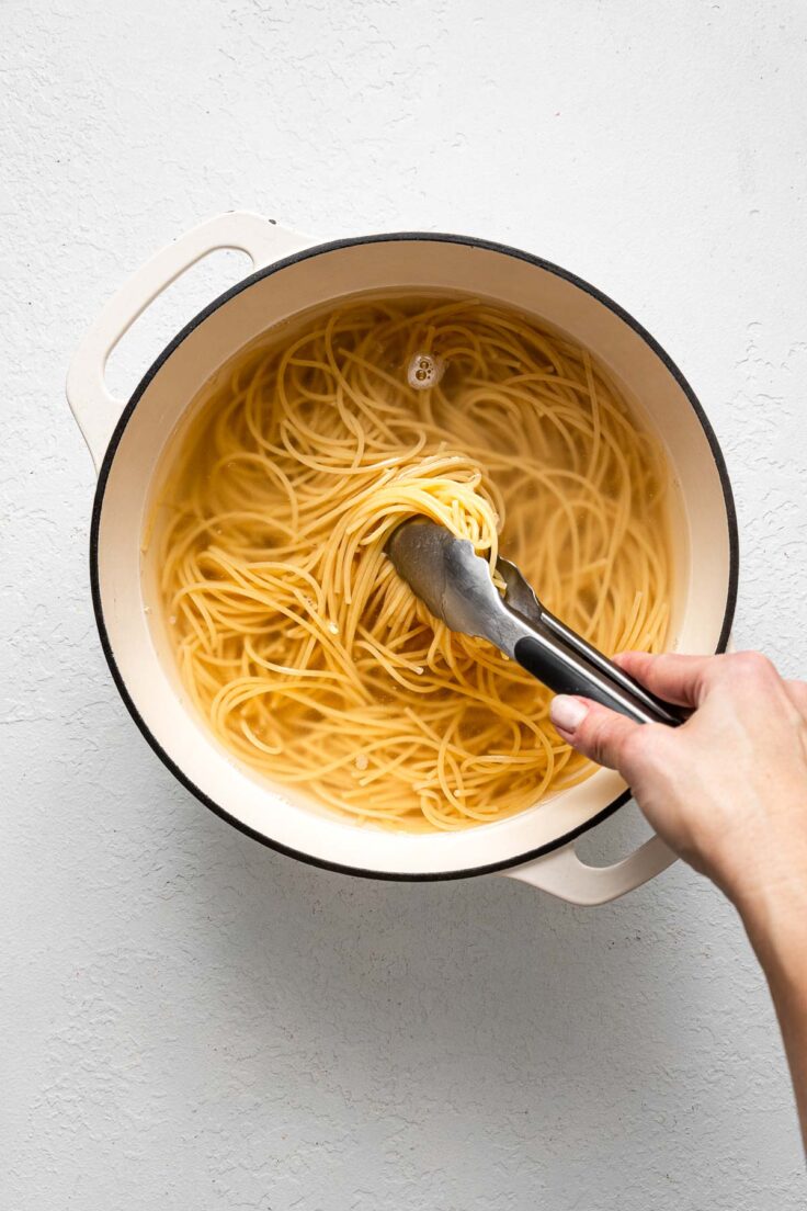 white pot of pasta and water being stirred with tongs.