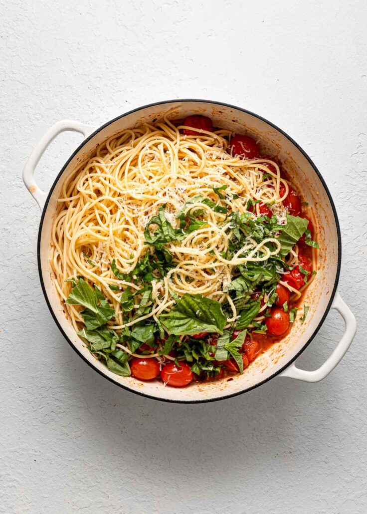 white pot with cooked spaghetti and basil added.