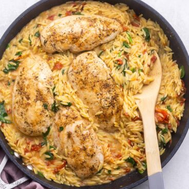close up shot of tuscan orzo and chicken in black pan.