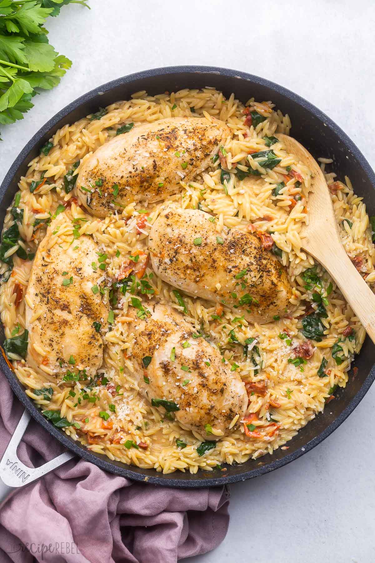 tuscan orzo with chicken in a black frying pan and a wooden ladle.