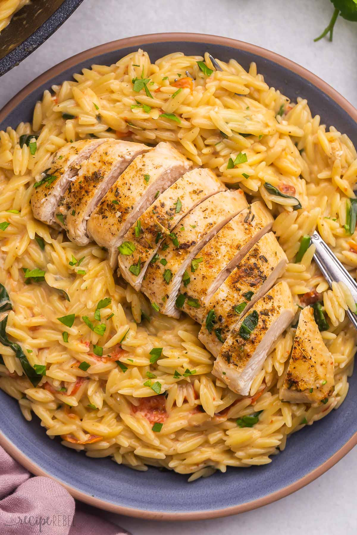 sliced chicken breast on a blue plate full of tuscan orzo.