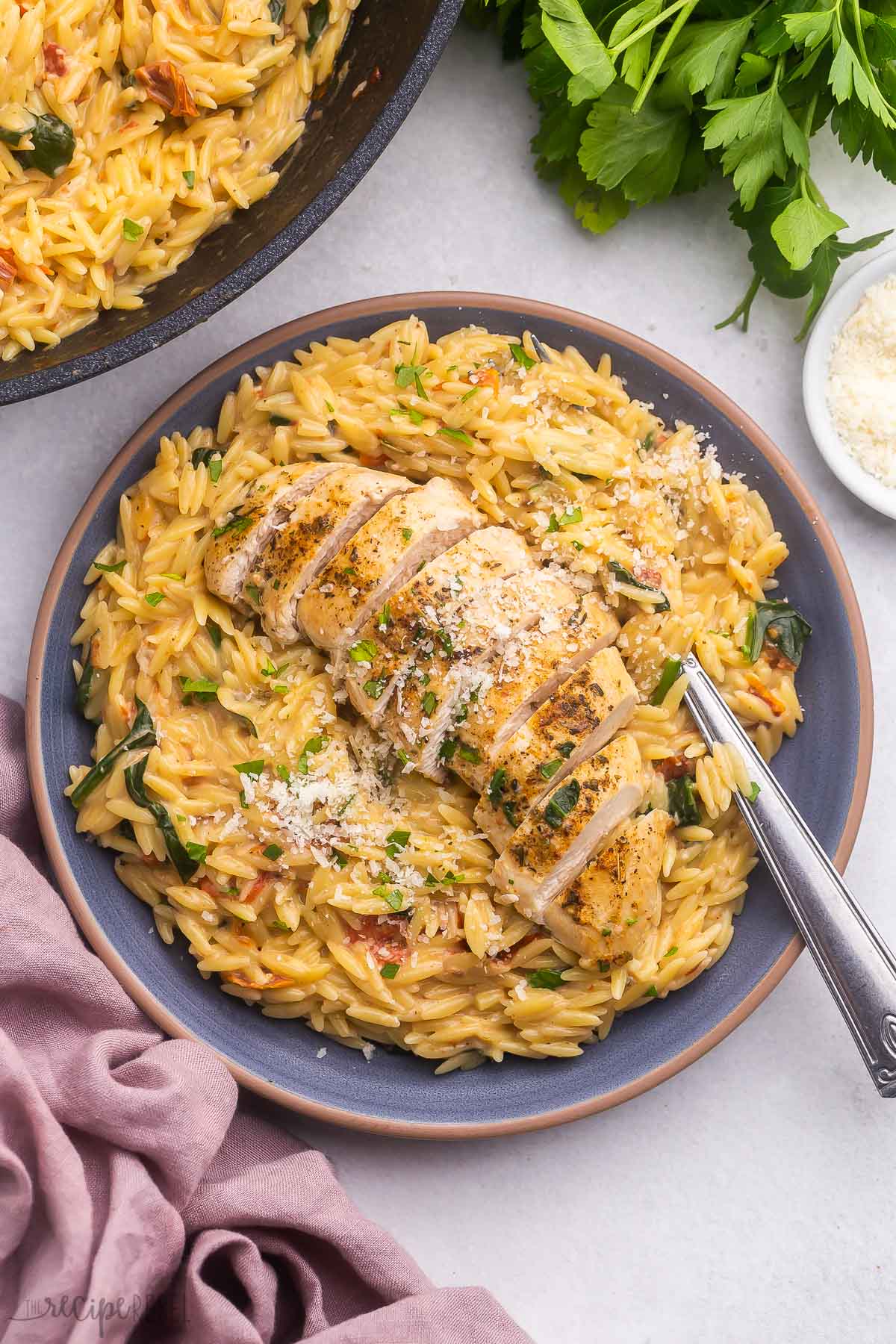 blue plate filled with tuscan orzo and chicken with a fork beside.