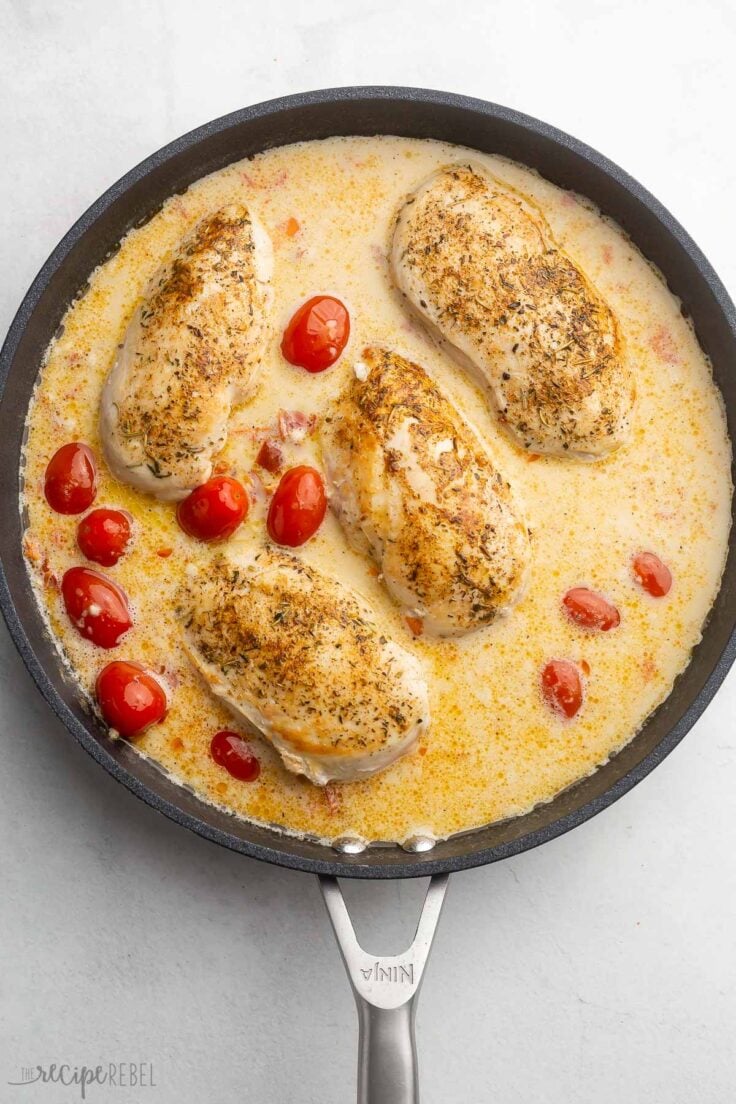 overhead shot of frying pan with sauce, tomatoes, and cooked chicken breasts added.