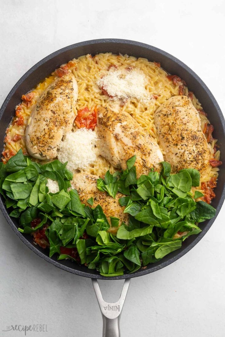 overhead shot of all tuscan chicken with orzo ingredients added into pan.