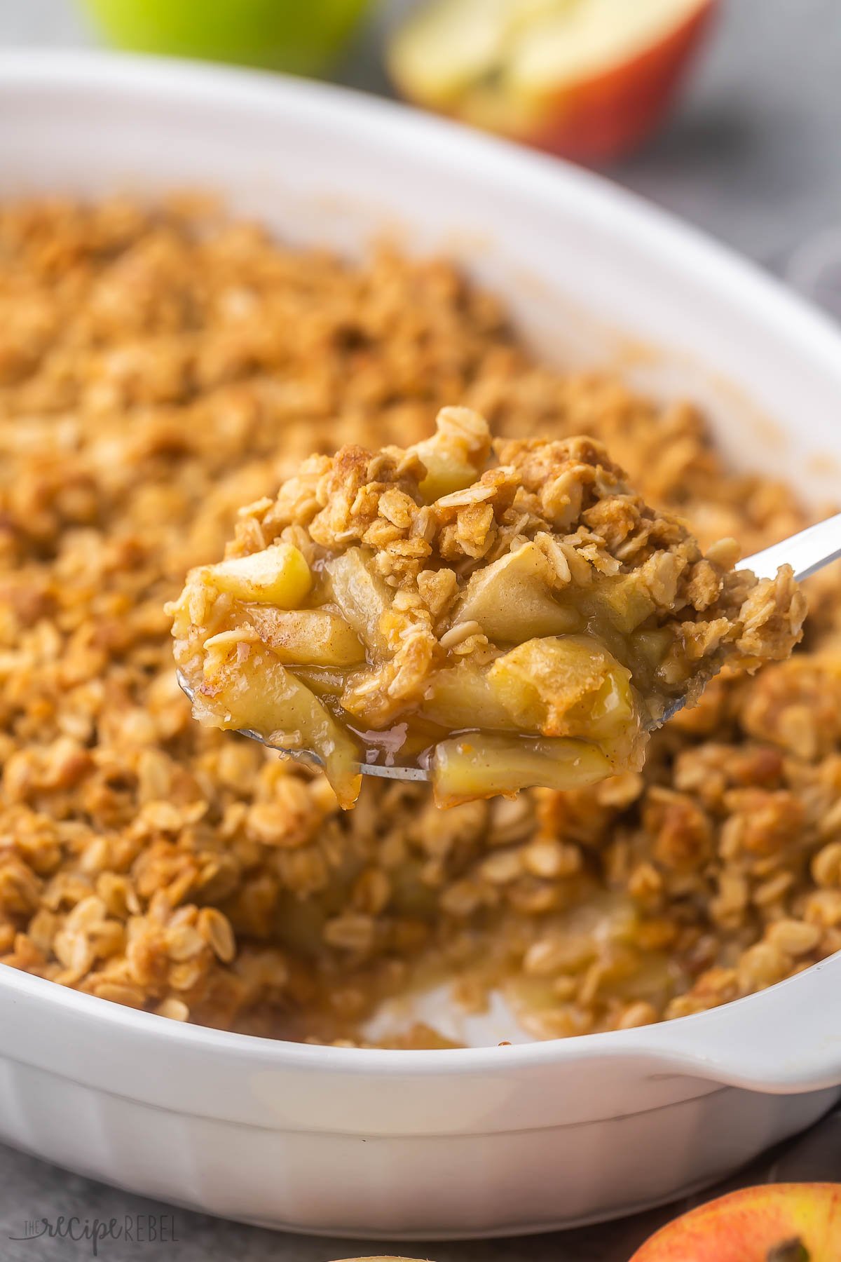 close up of a steel spoon scooping apple crisp out of white dish.