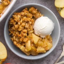 close up view of a bowl filled with apple crisp and a scoop of vanilla ice cream on the side.
