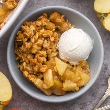 close up view of a bowl filled with apple crisp and a scoop of vanilla ice cream on the side.