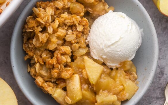 close up view of a bowl filled with apple crisp and a scoop of vanilla ice cream on the side.