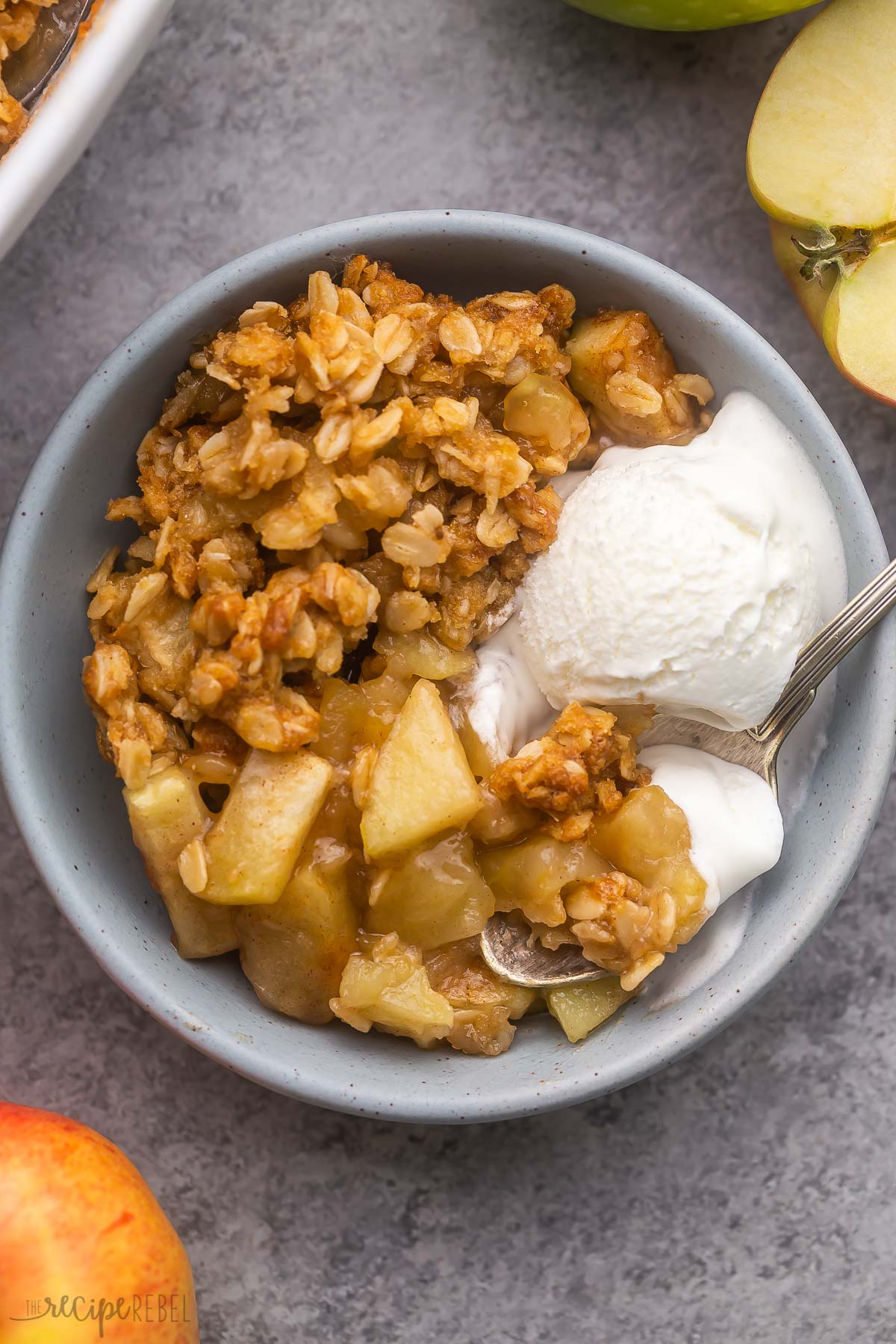 a spoon scooping ice cream and apple crisp out of a blue bowl.