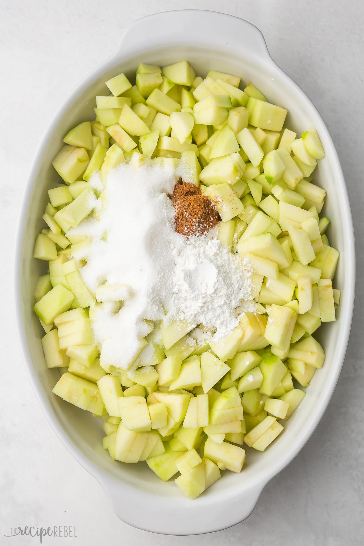 white baking dish filled with green apples, sugar, corn starch and cinnamon.